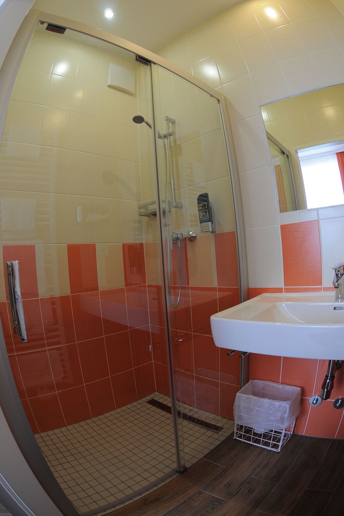 Koupelna se sprchovým koutem, umyvadlem a oranžovo-bílými obklady.