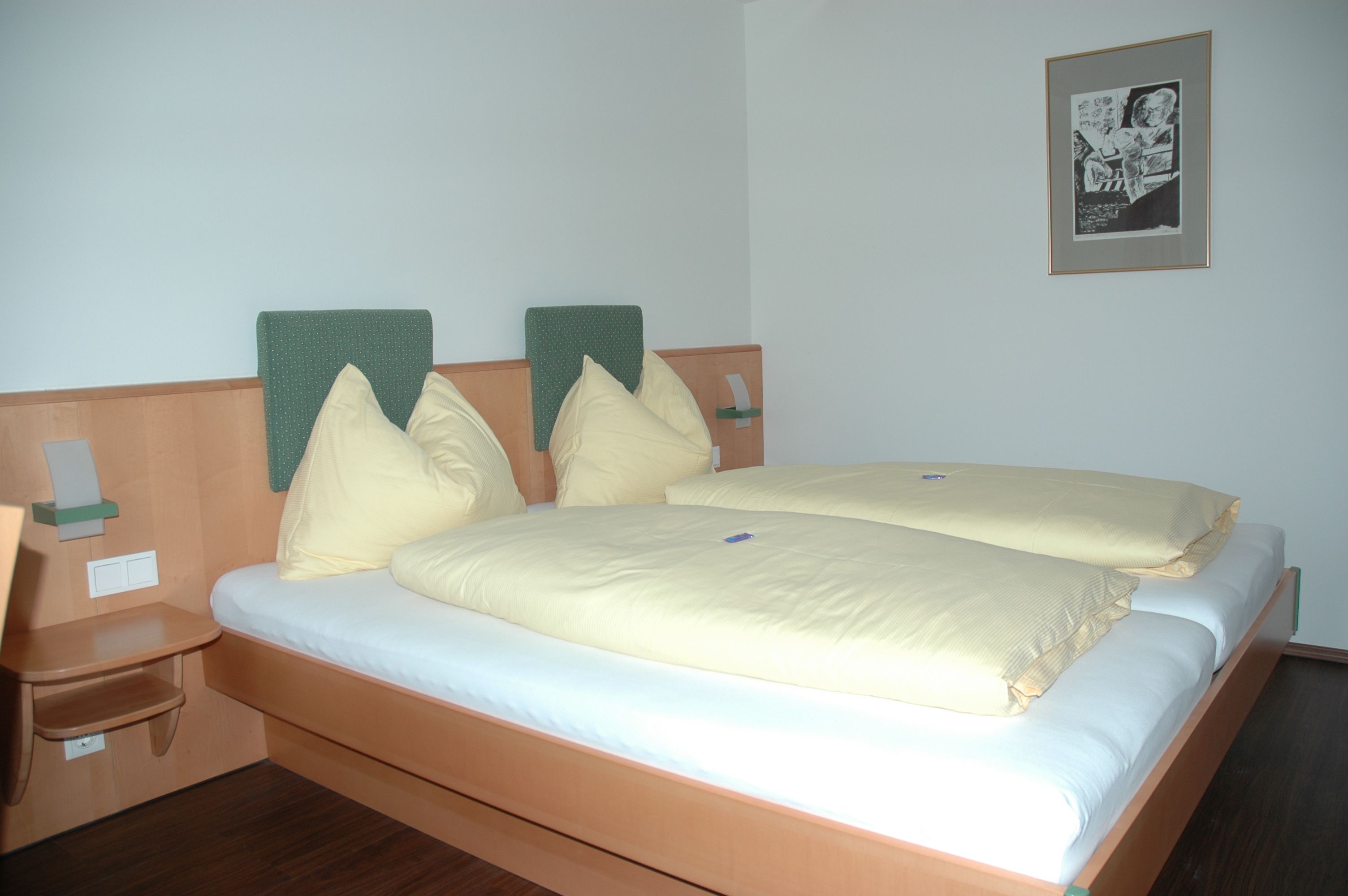 Hotelový pokoj s manželskou postelí, žlutým ložním prádlem a nástěnnou malbou.