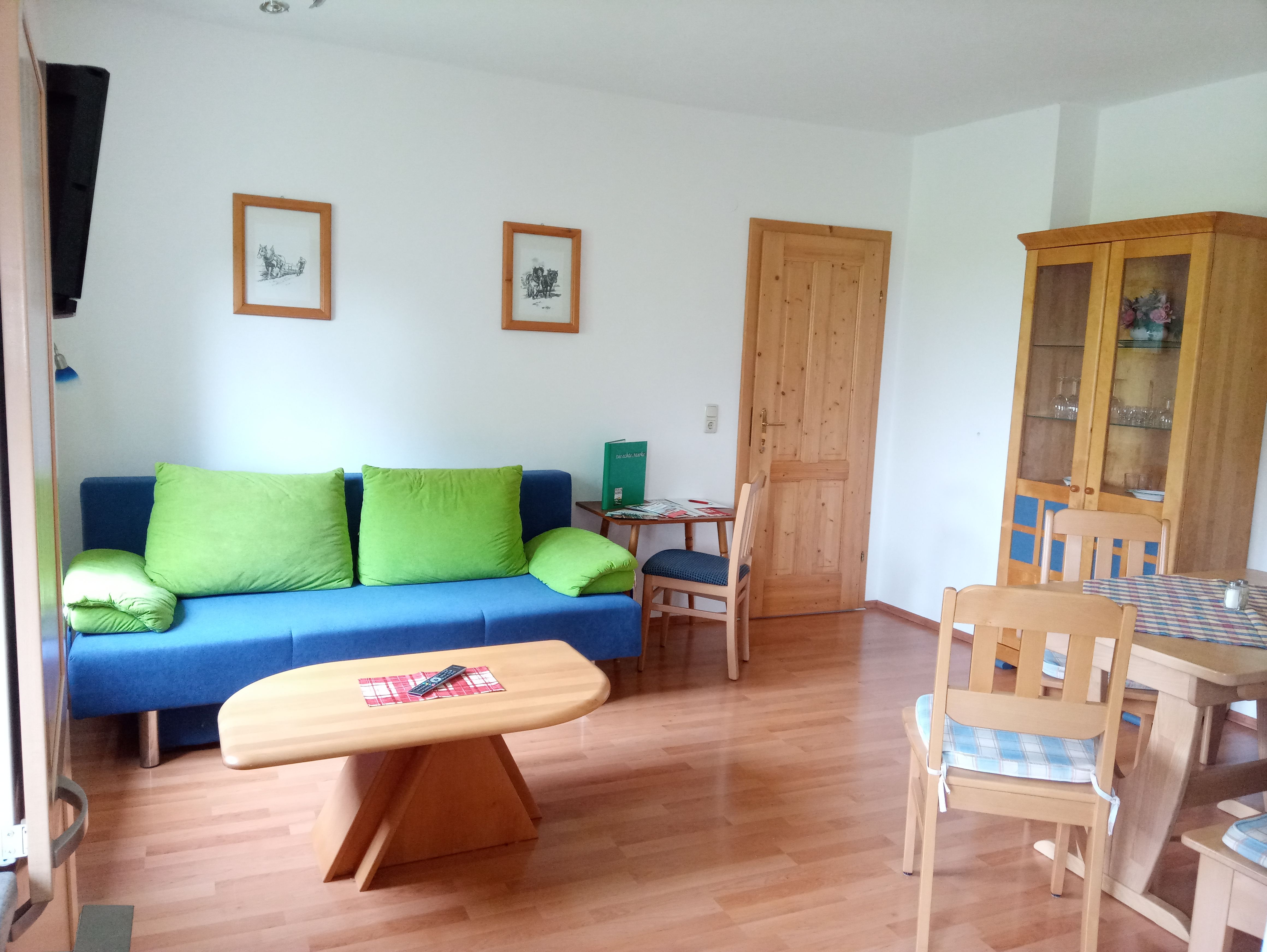 Obývací pokoj s modrou pohovkou, dřevěným stolem a židlemi, šatní skříní a obrazy na stěně.