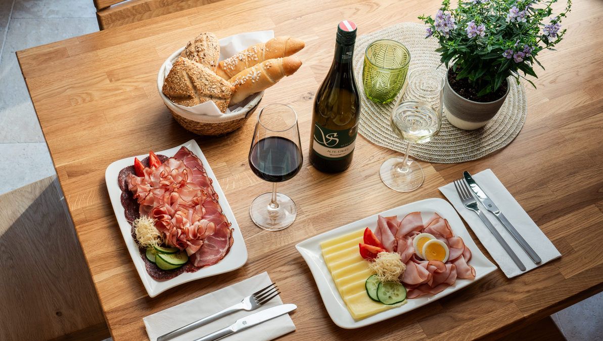 Stůl s regionálními pochoutkami: V nabídce jsou uzeniny, sýry, chléb, červené a bílé víno.