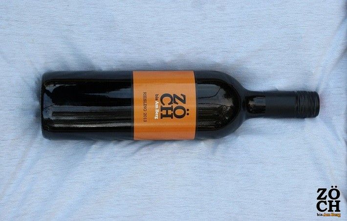Láhev vína s oranžovou etiketou značky Zöch na světlém pozadí.