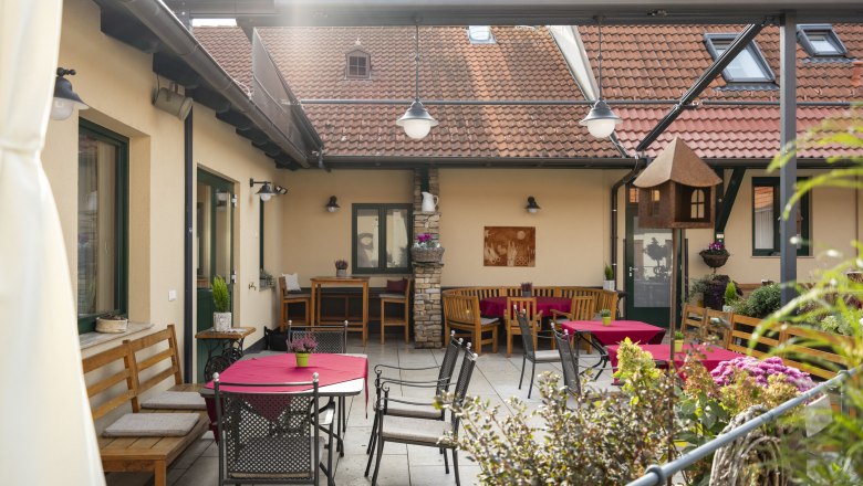 Útulný vnitřní dvůr s posezením a červenými ubrusy.