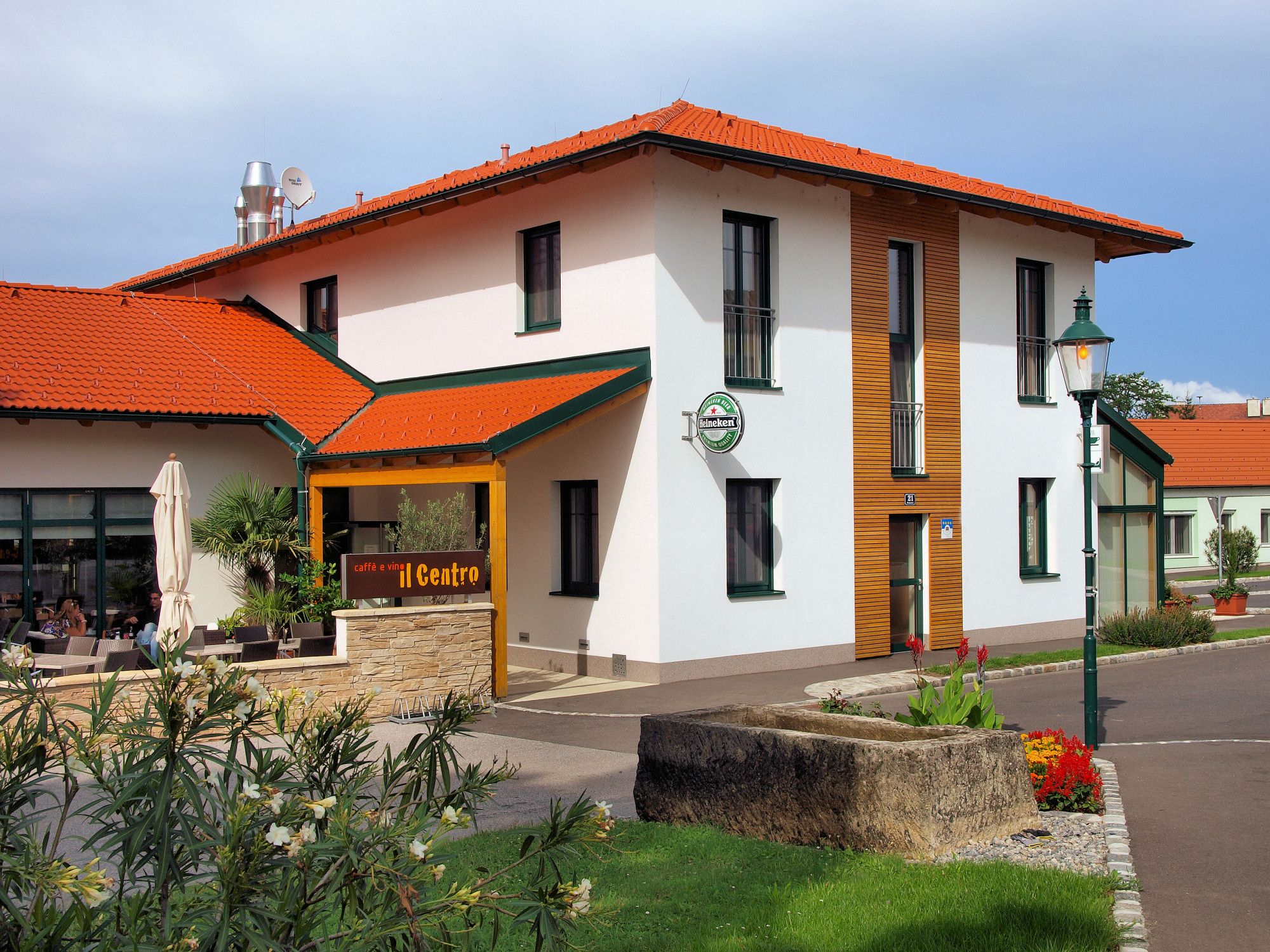 Pohled zvenčí na budovu s červenou střechou a terasou s nápisem "caffè e vini Centro".