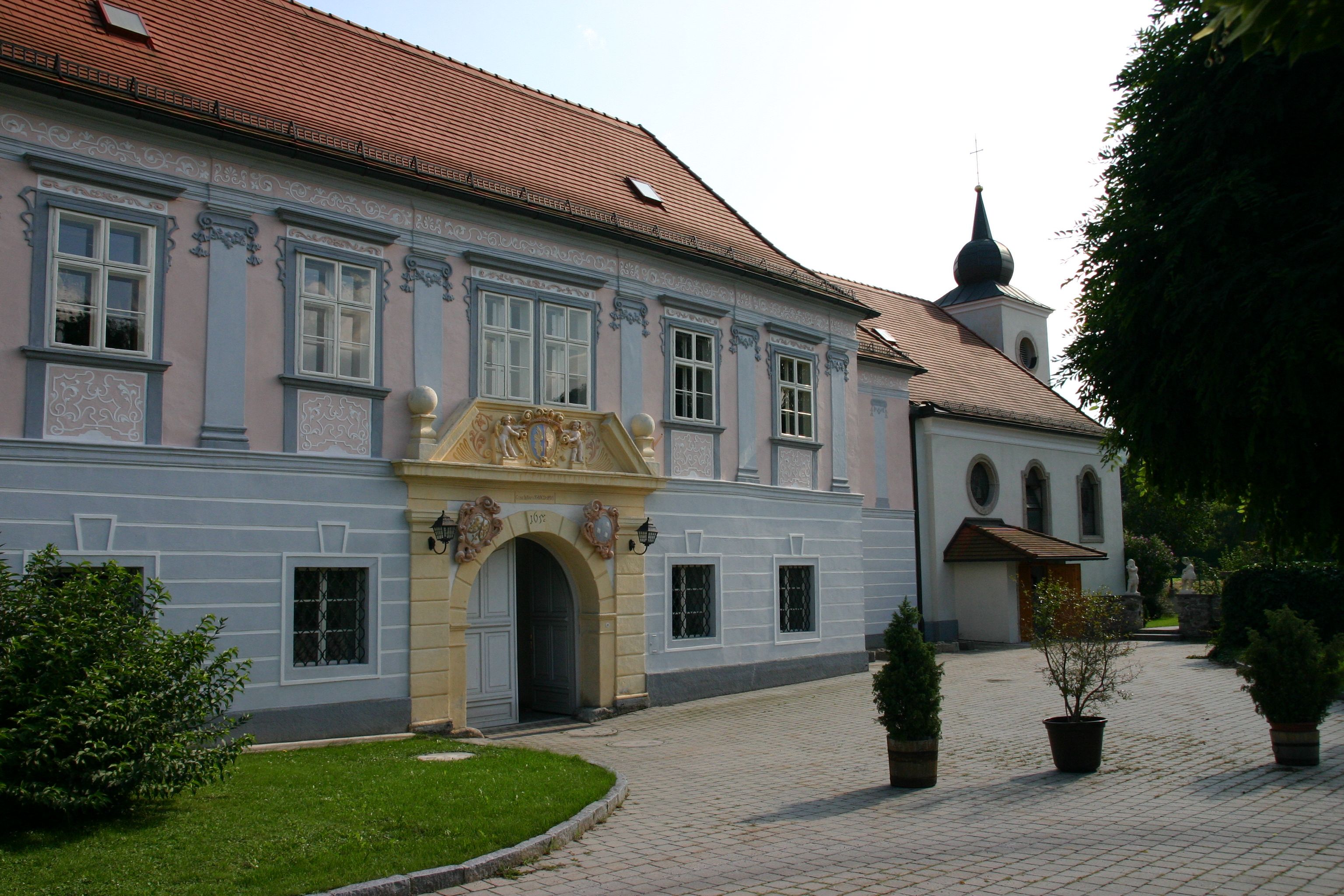 Historická budova se zdobeným vchodem a kostelem v pozadí.