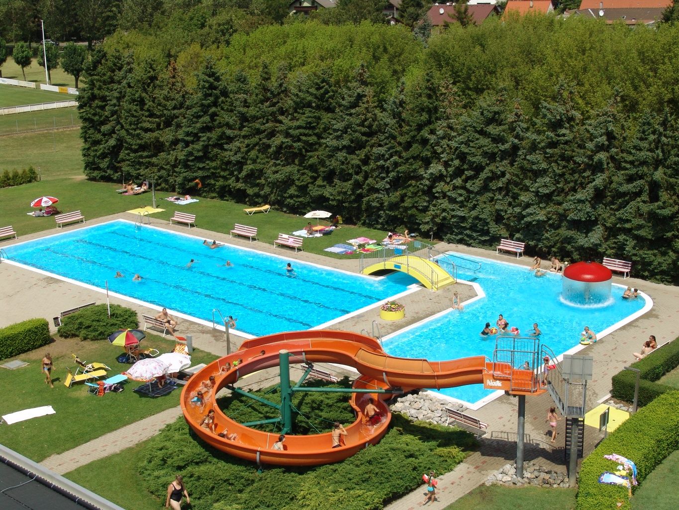 Letecký pohled na venkovní bazén se skluzavkou, dvěma bazény a plochou na opalování.