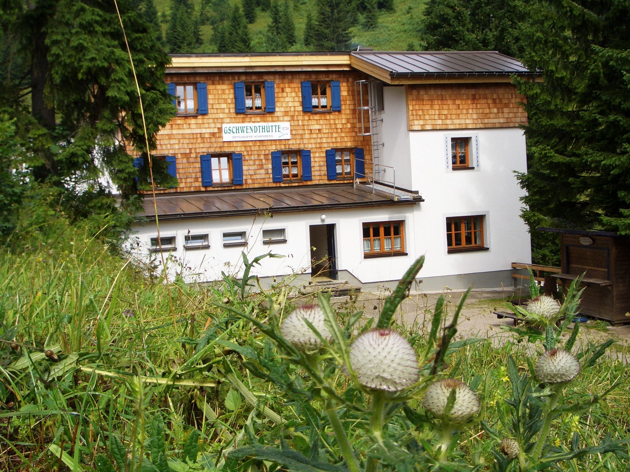 Gschwendthütte v Hohenbergu, obklopená zelenou přírodou a stromy.