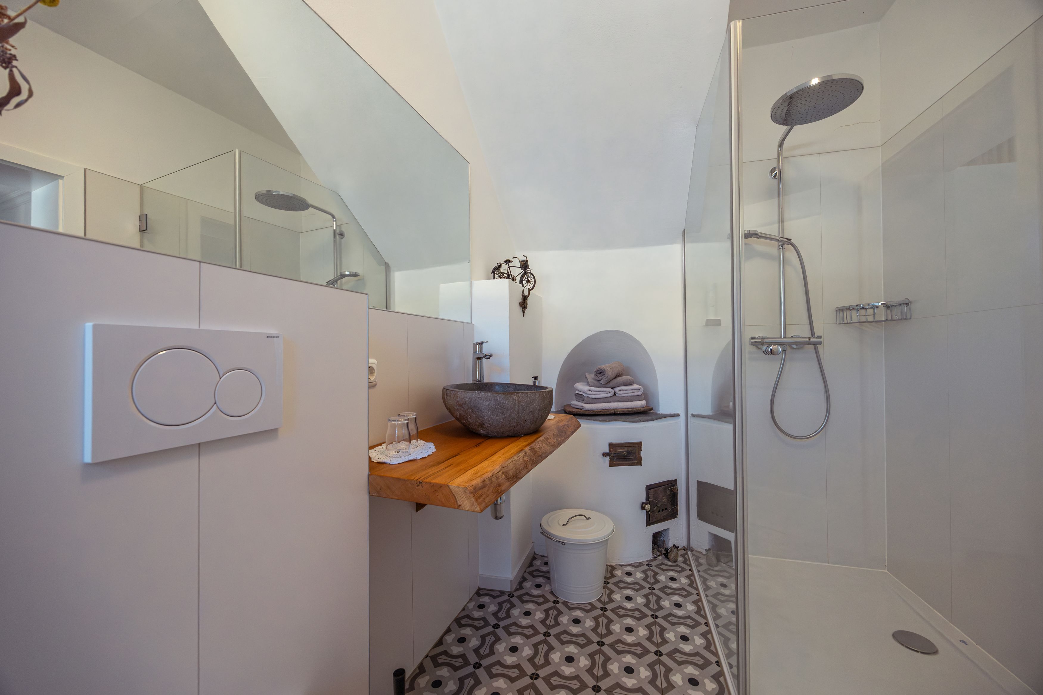 Moderní koupelna se skleněným sprchovým koutem, kamenným umyvadlem a vzorovanou podlahou.