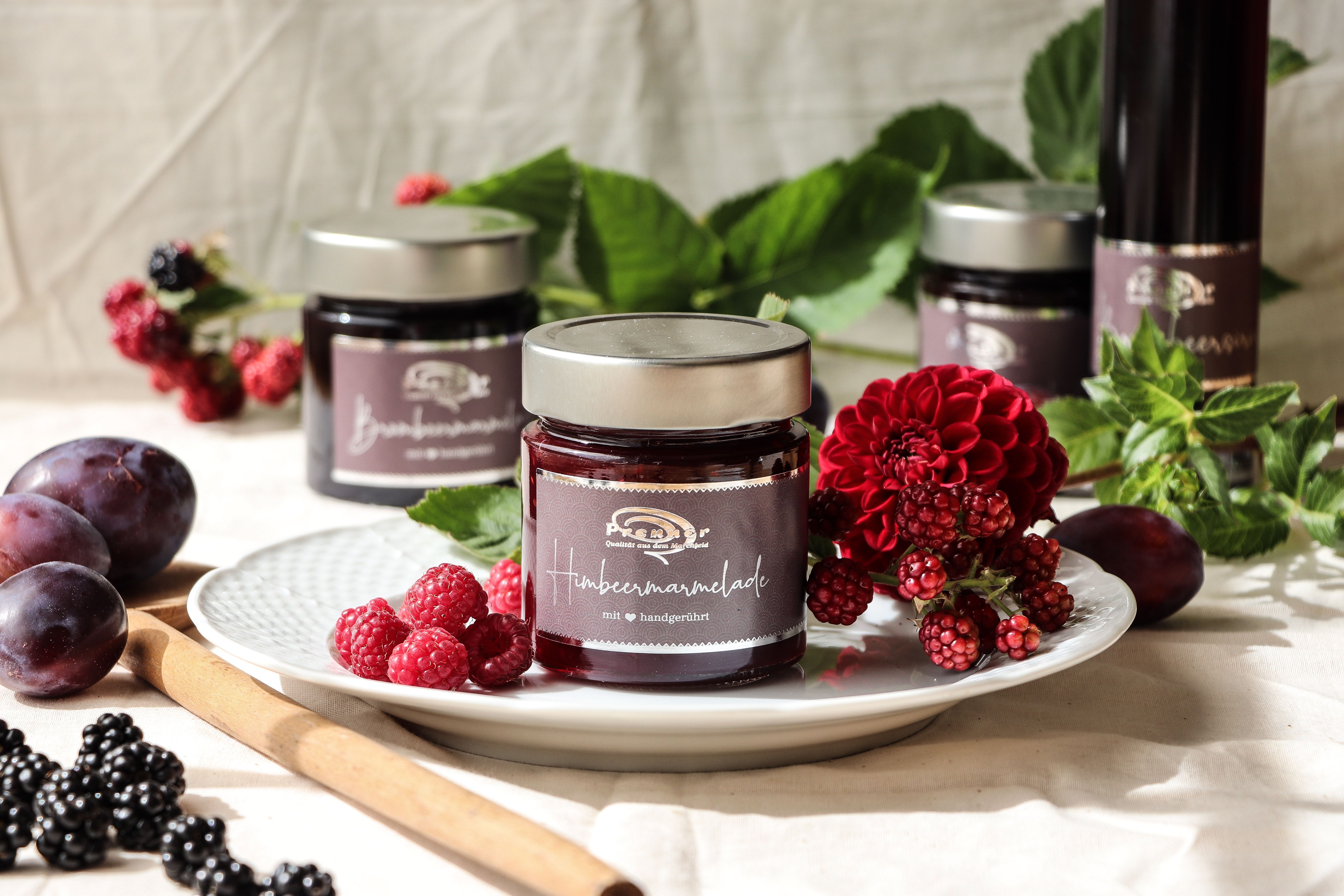 Sklenice malinové marmelády na talíři zdobeném čerstvými bobulemi a květinami.