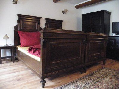 Dřevěná postel v rustikální ložnici s červeným ložním prádlem.