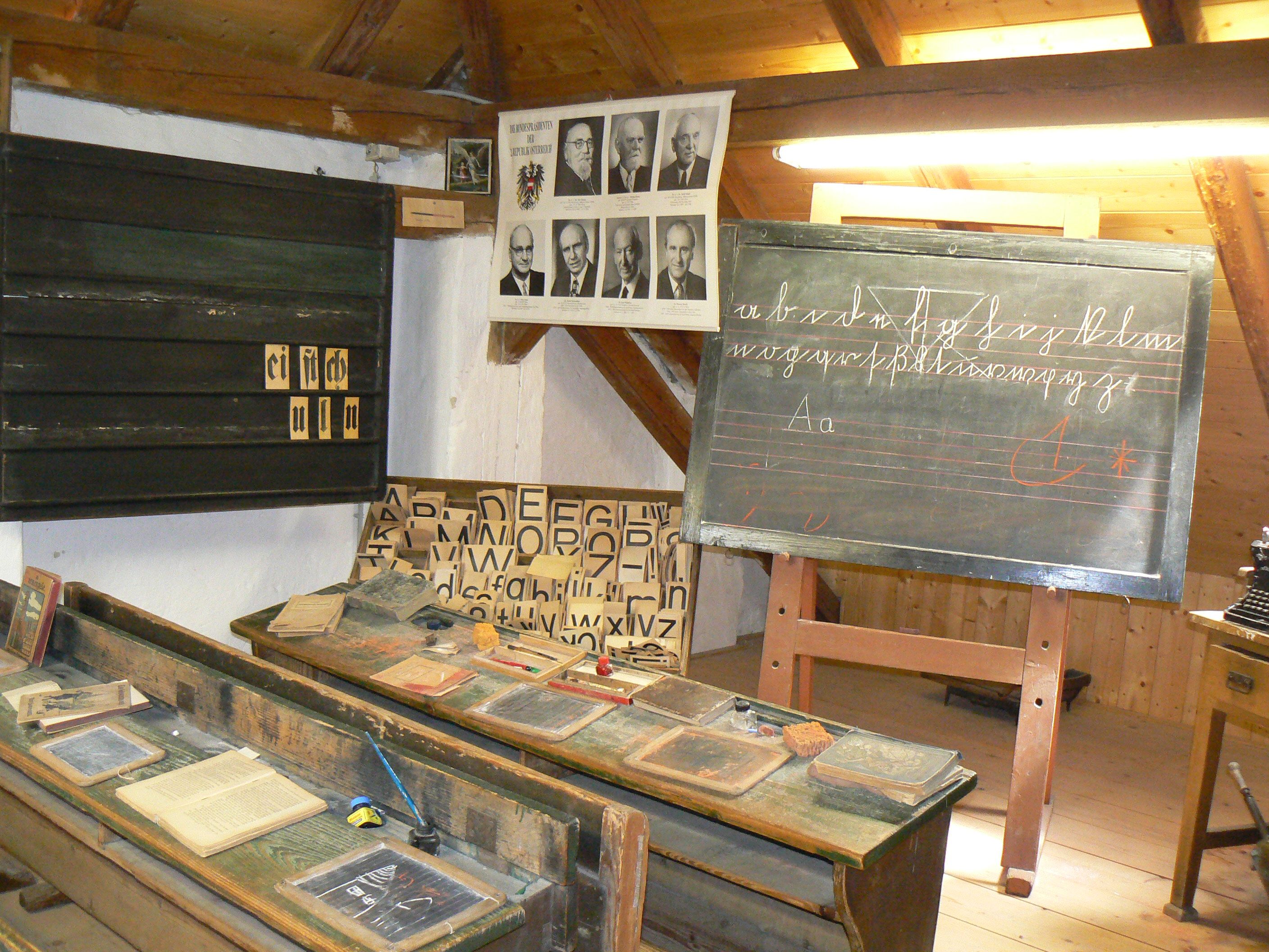 Historická učebna s tabulí, stolem a učebními pomůckami.