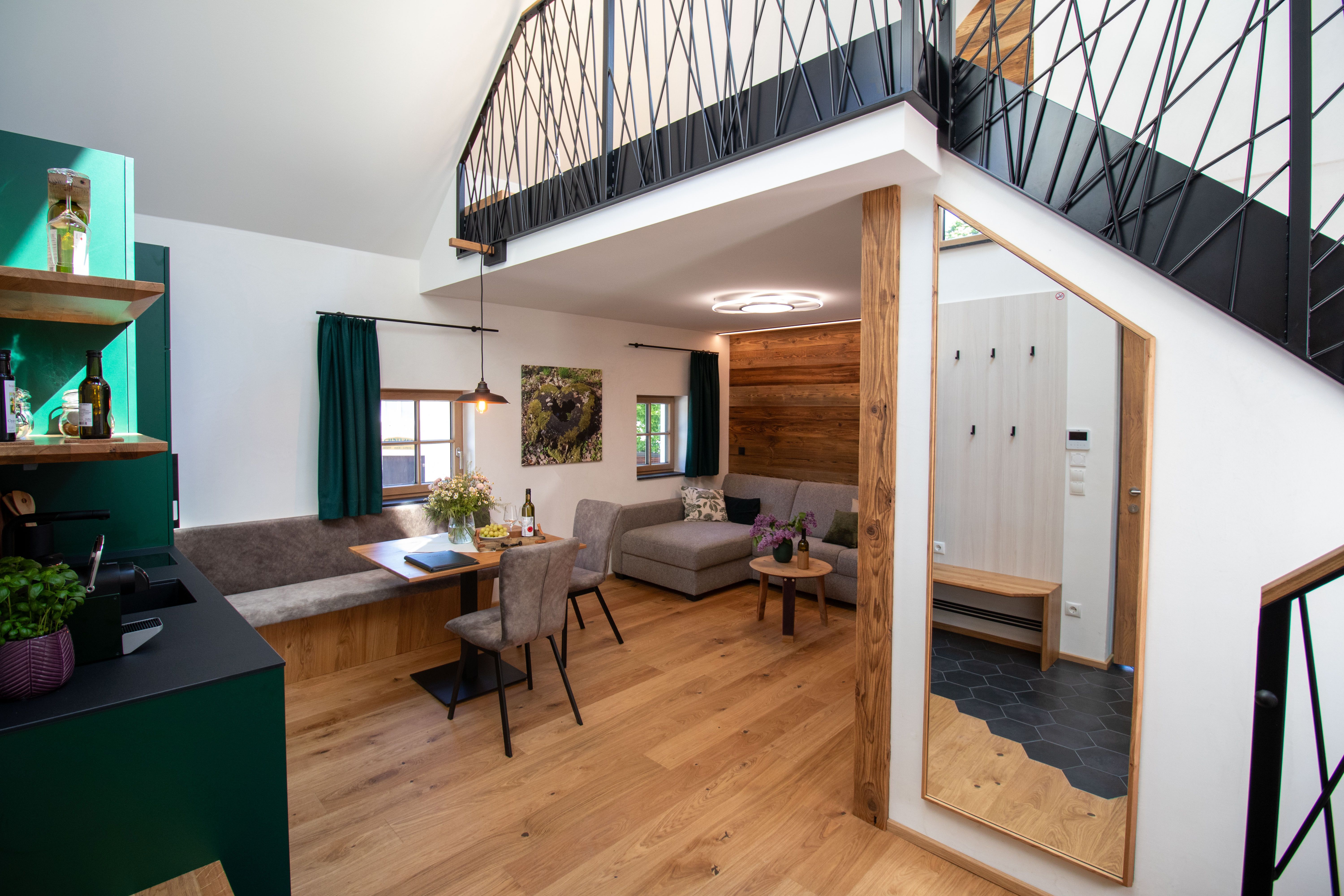 Moderní byt s dřevěnou podlahou, šedou pohovkou, jídelním stolem a otevřenou galerií.