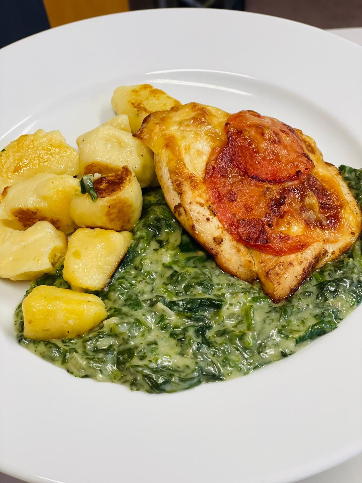 Talíř s gnocchi, krémovým špenátem a zapečeným kuřetem s plátkem rajčete.