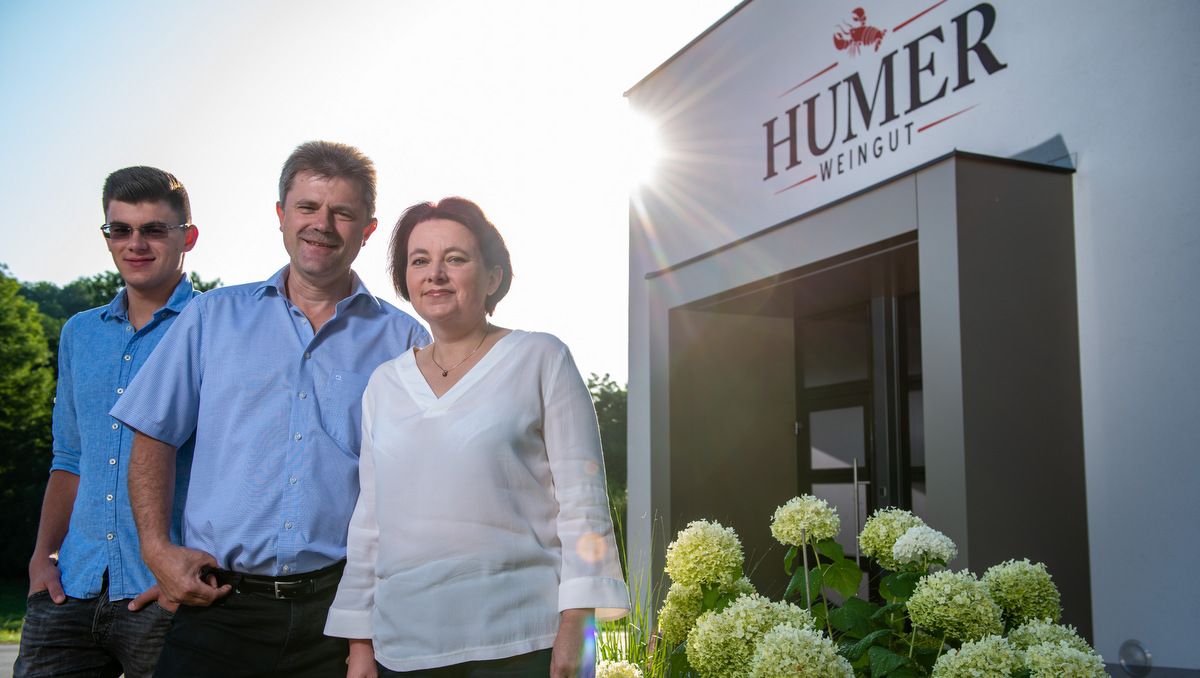 Tři lidé před vchodem do vinařství Humer, obklopeni květinami.