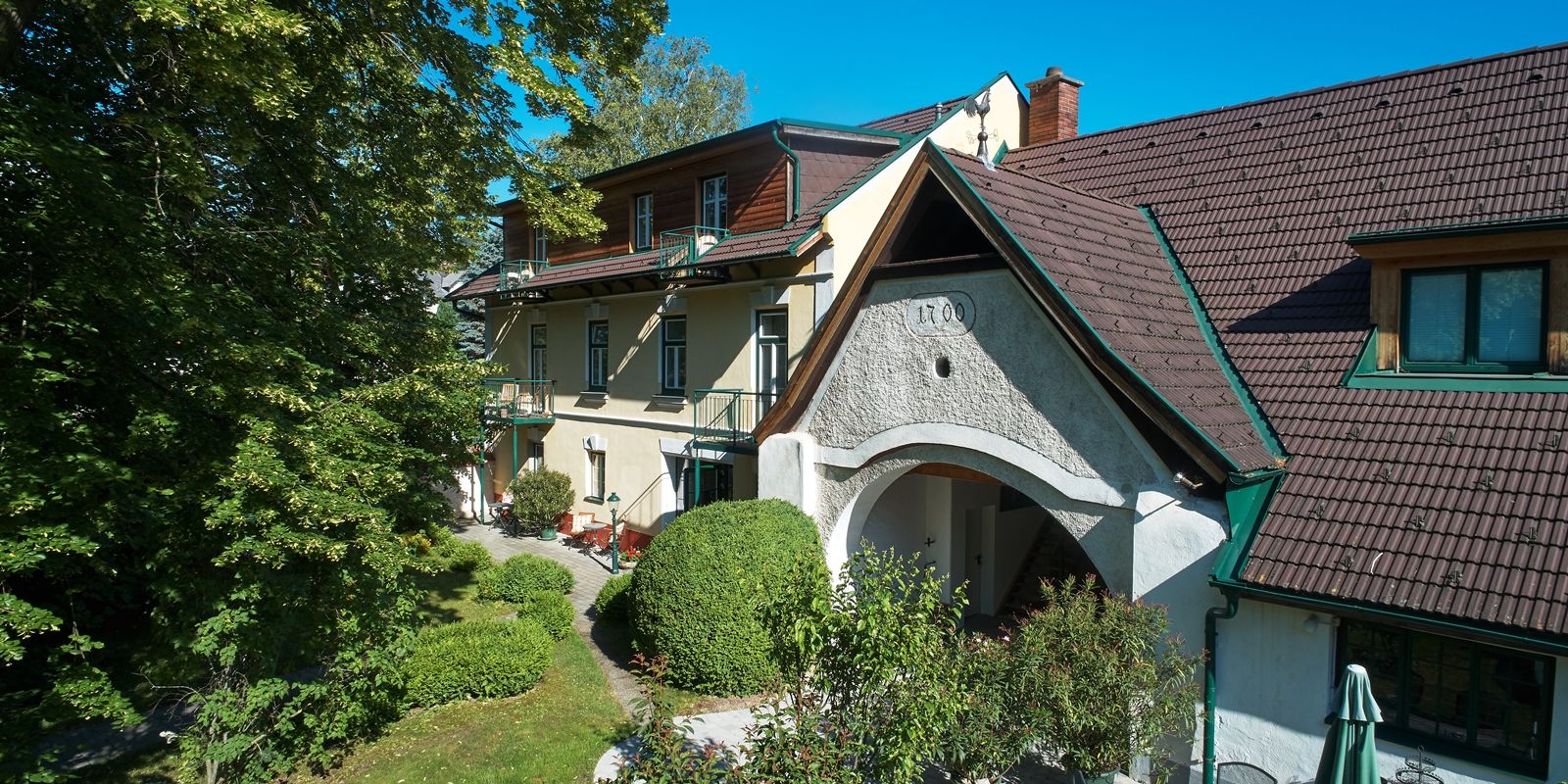 Landhaus Puchbergerhof se zahradou a stromy v popředí.