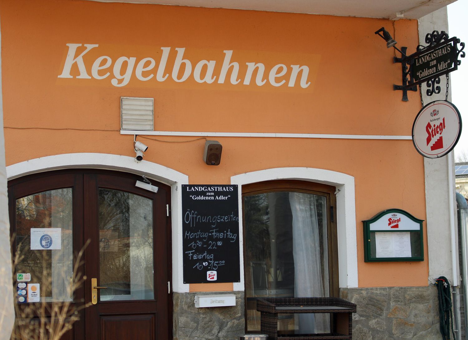 Vchod do venkovského hostince s nápisem "Kegelbahnen" a cedulí s pivem Stiegl.