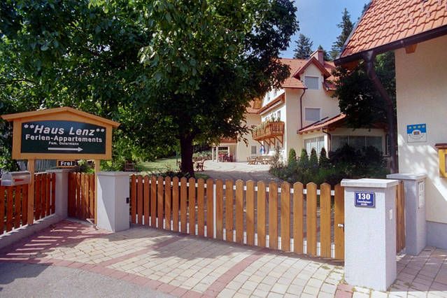 Vchod do domu Haus Lenz s dřevěným plotem a cedulí, obklopený stromy.