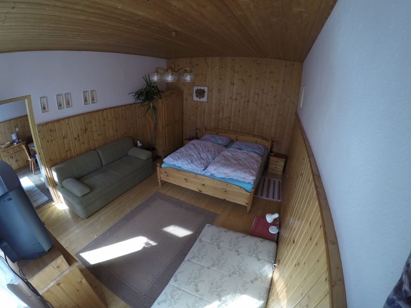 Útulná ložnice s dřevěnými stěnami, manželskou postelí, pohovkou a kobercem na dřevěné podlaze.
