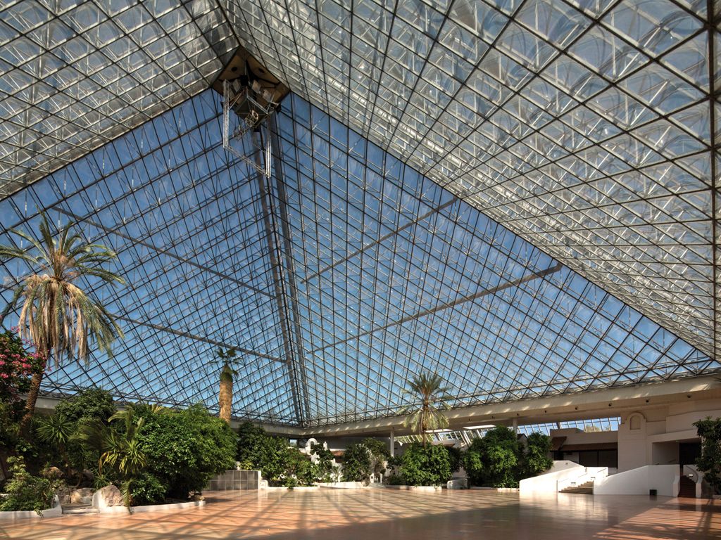 Pohled do interiéru velké skleněné pyramidy s rostlinami a palmami.