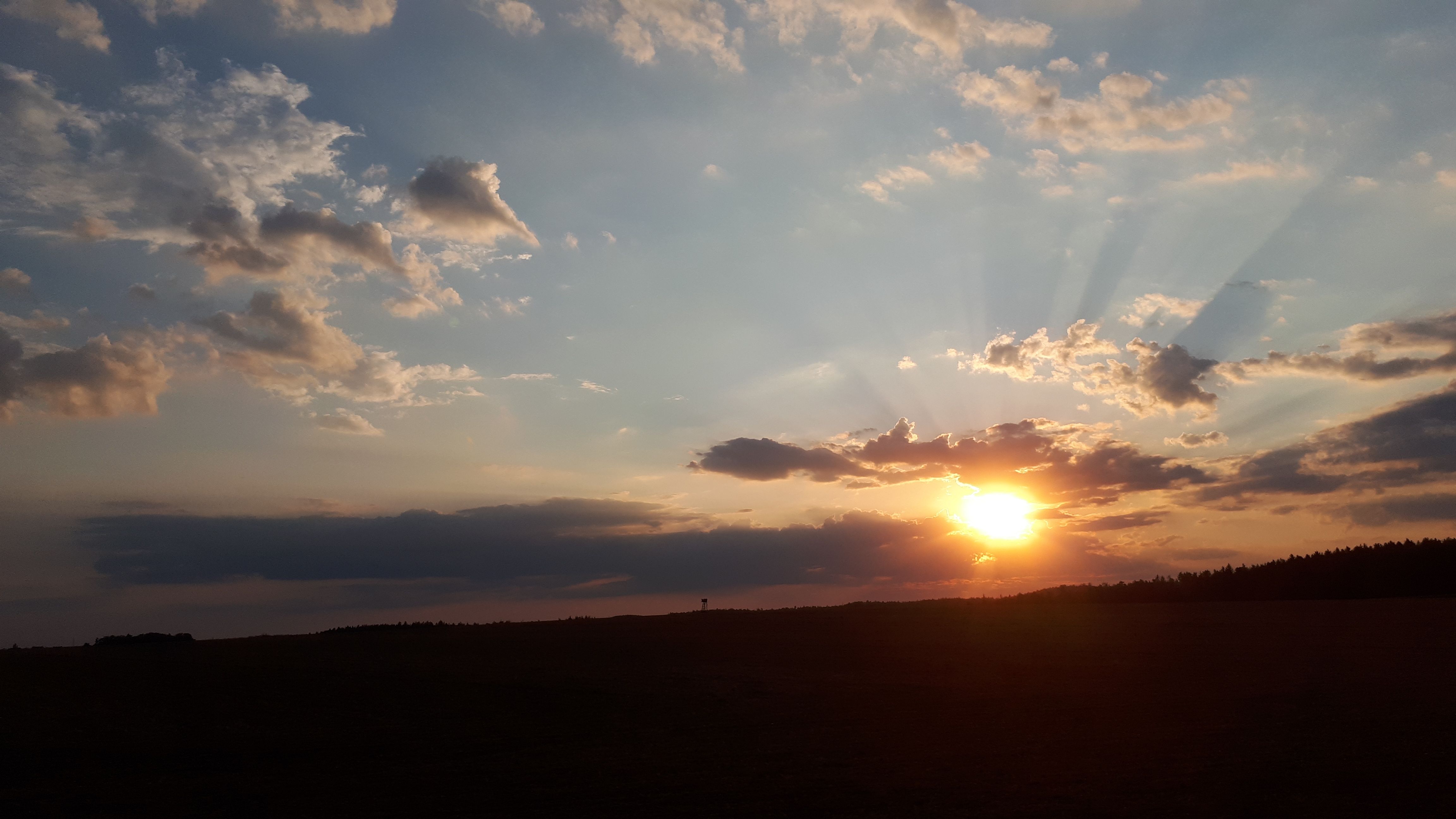 Západ slunce s mraky a paprsky na obloze.