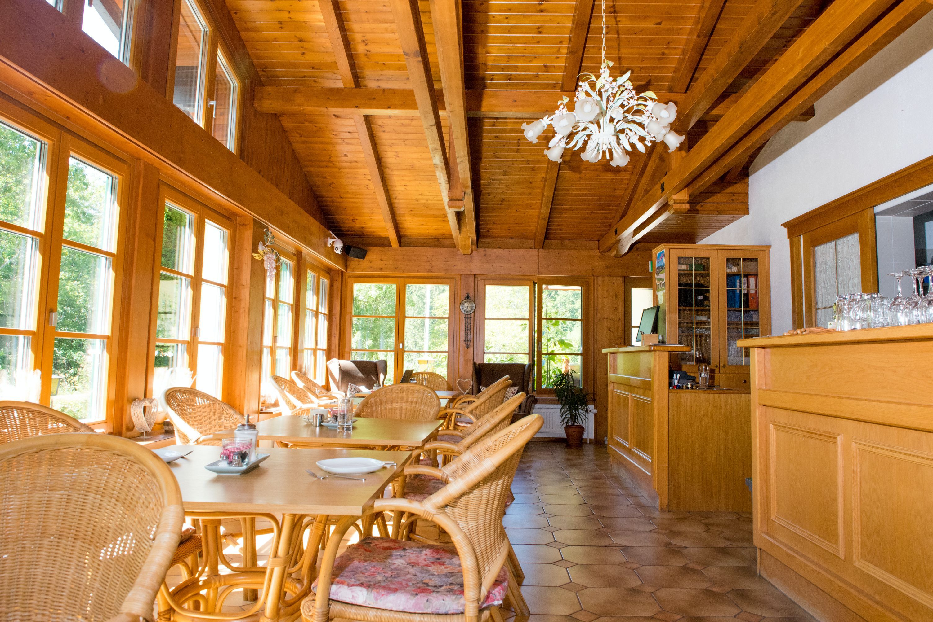 Světlá snídaňová místnost s dřevěným nábytkem, velkými okny a lustrem.