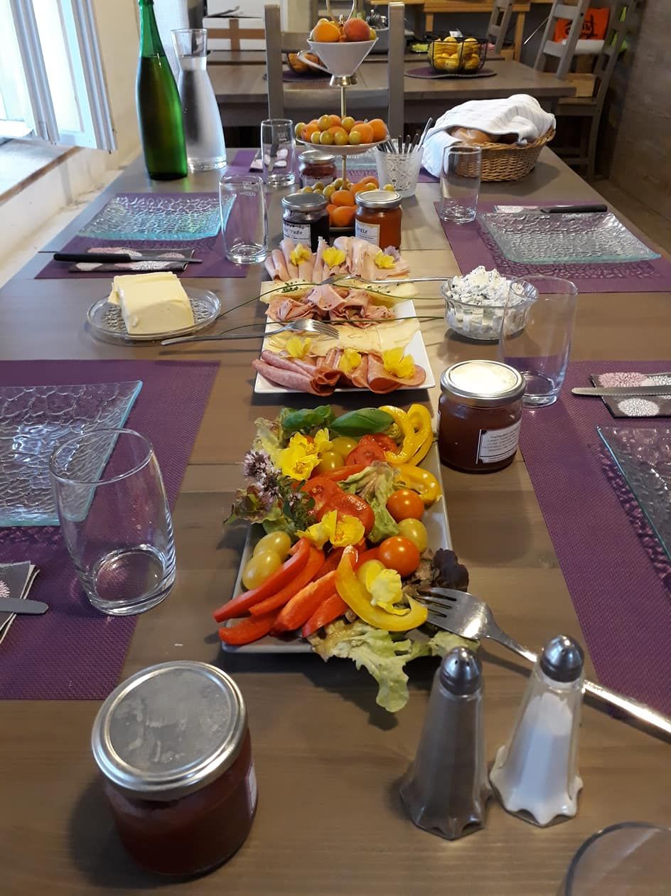 Prostřený snídaňový stůl s uzeninami, zeleninou, džemem a nápoji.