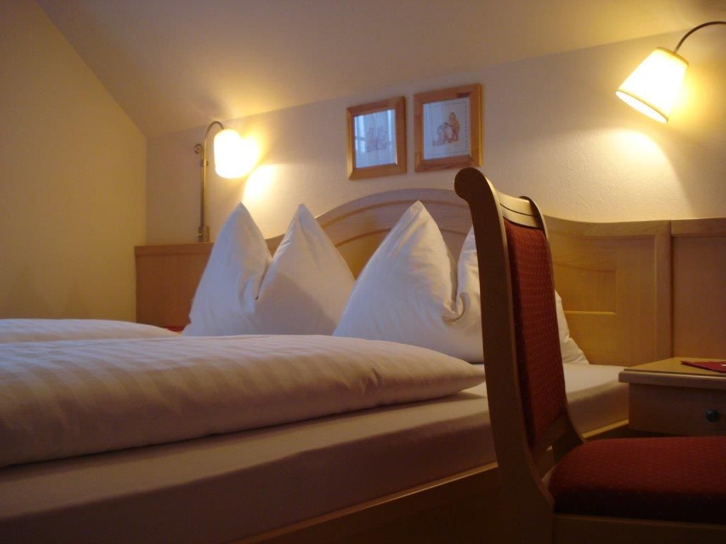 Útulný pokoj pro hosty s manželskou postelí, dvěma nočními lampičkami a židlí.