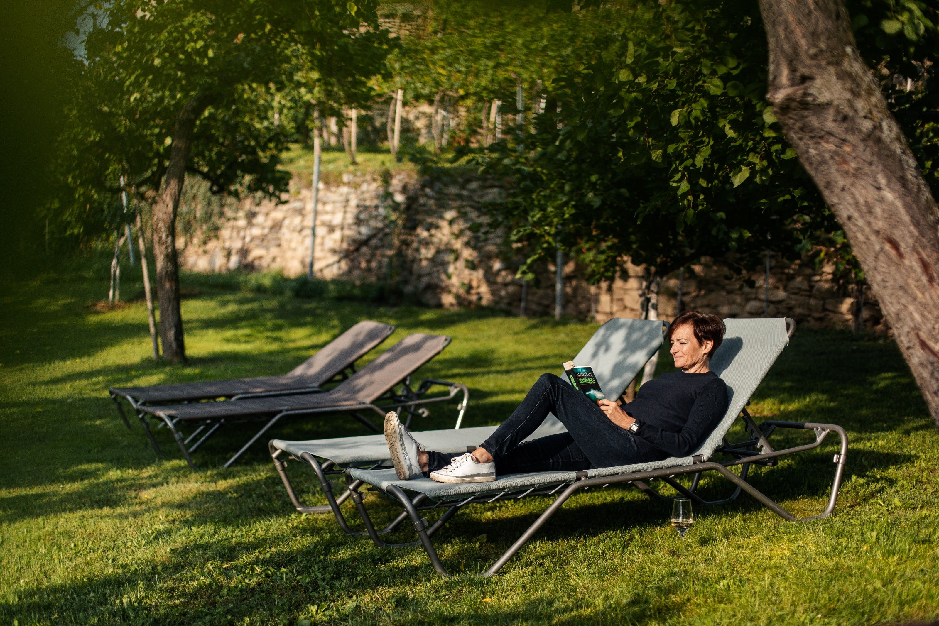 Osoba si čte na lehátku na zahradě.