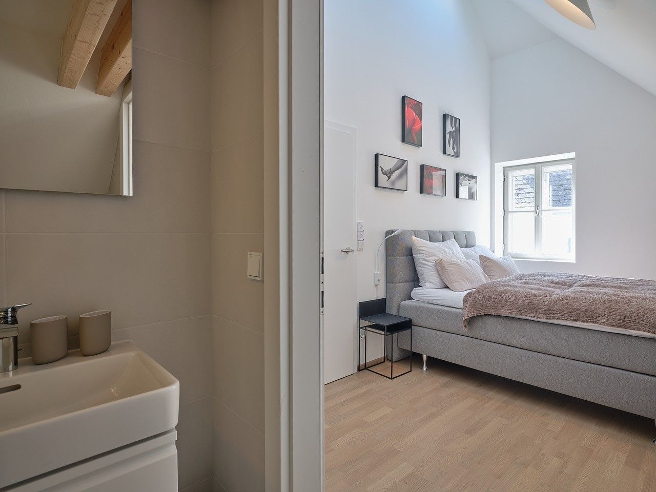 Moderní ložnice s šedou postelí a přilehlou koupelnou.