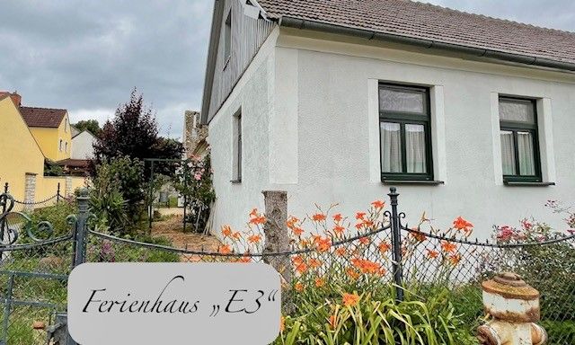 Pohled zvenčí na bílý rekreační dům se zahradou a květinami.