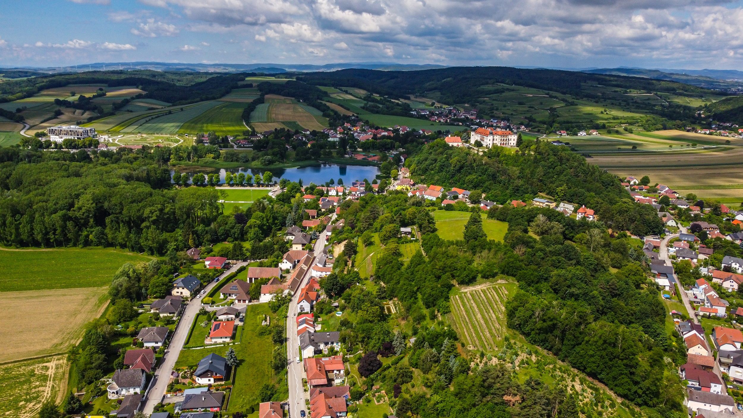 Letecký pohled na venkovskou oblast s poli, jezerem a hradem na kopci.