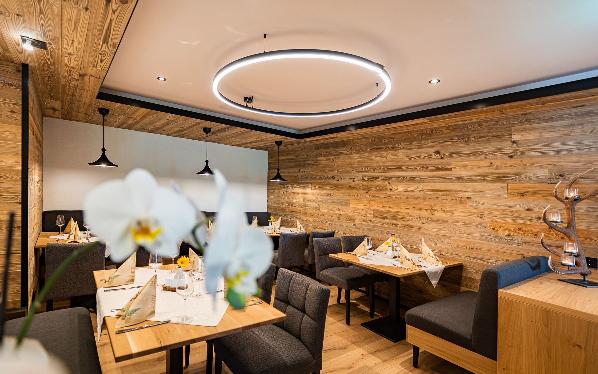 Útulná restaurace s dřevěnými stěnami, moderním osvětlením a elegantně prostřenými stoly.