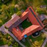 Letecký pohled na farmu s červenými střechami a solárními panely, obklopenou zelenými loukami a stromy.