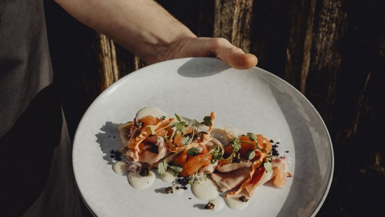 Jednou rukou se podává talíř s umně naaranžovaným vitello forello, ozdobený bylinkami a omáčkou.