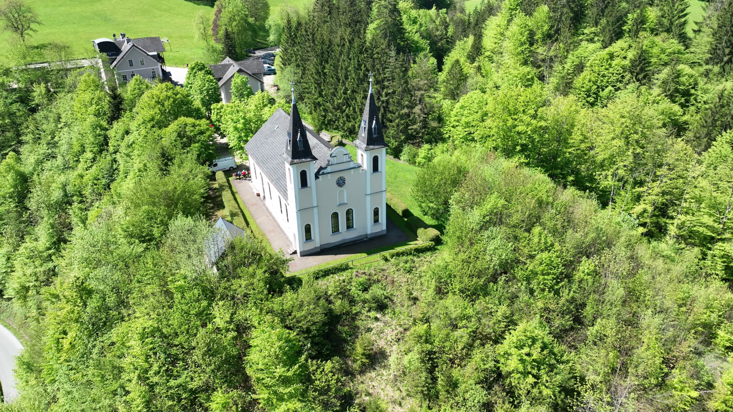 Letecký snímek poutního kostela Maria Seesal obklopeného zelenými stromy a lesy.