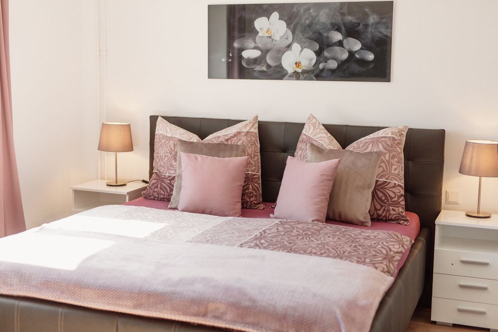 Útulná ložnice s manželskou postelí, růžovým ložním prádlem a dvěma nočními stolky s lampičkami.