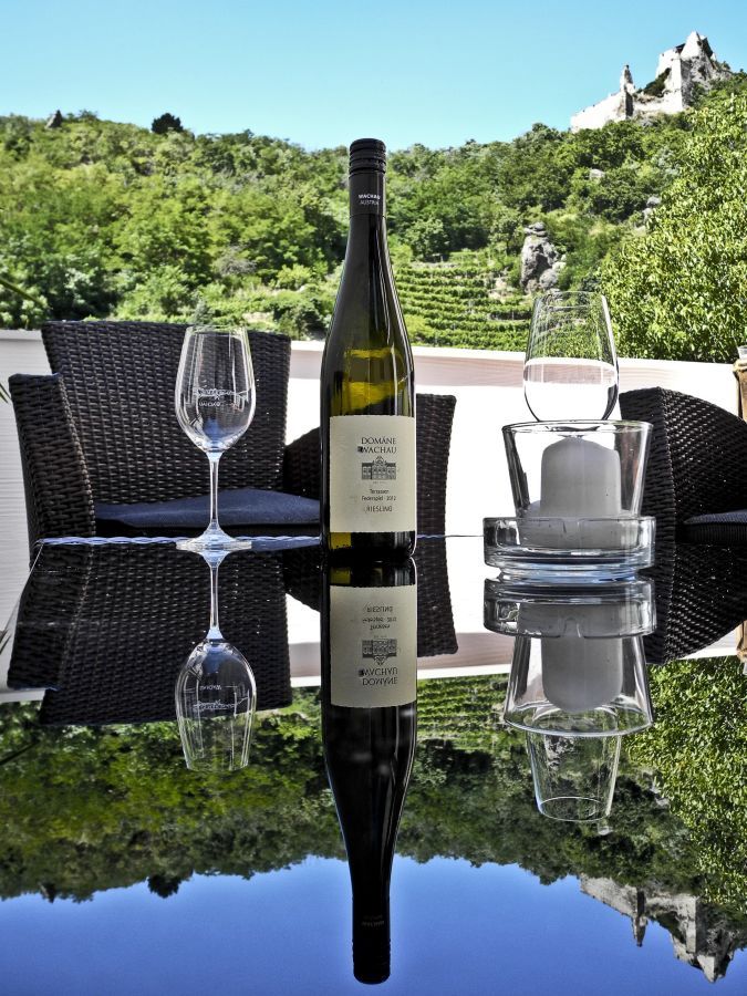 Láhev vína a sklenice na stole s výhledem na vinice.