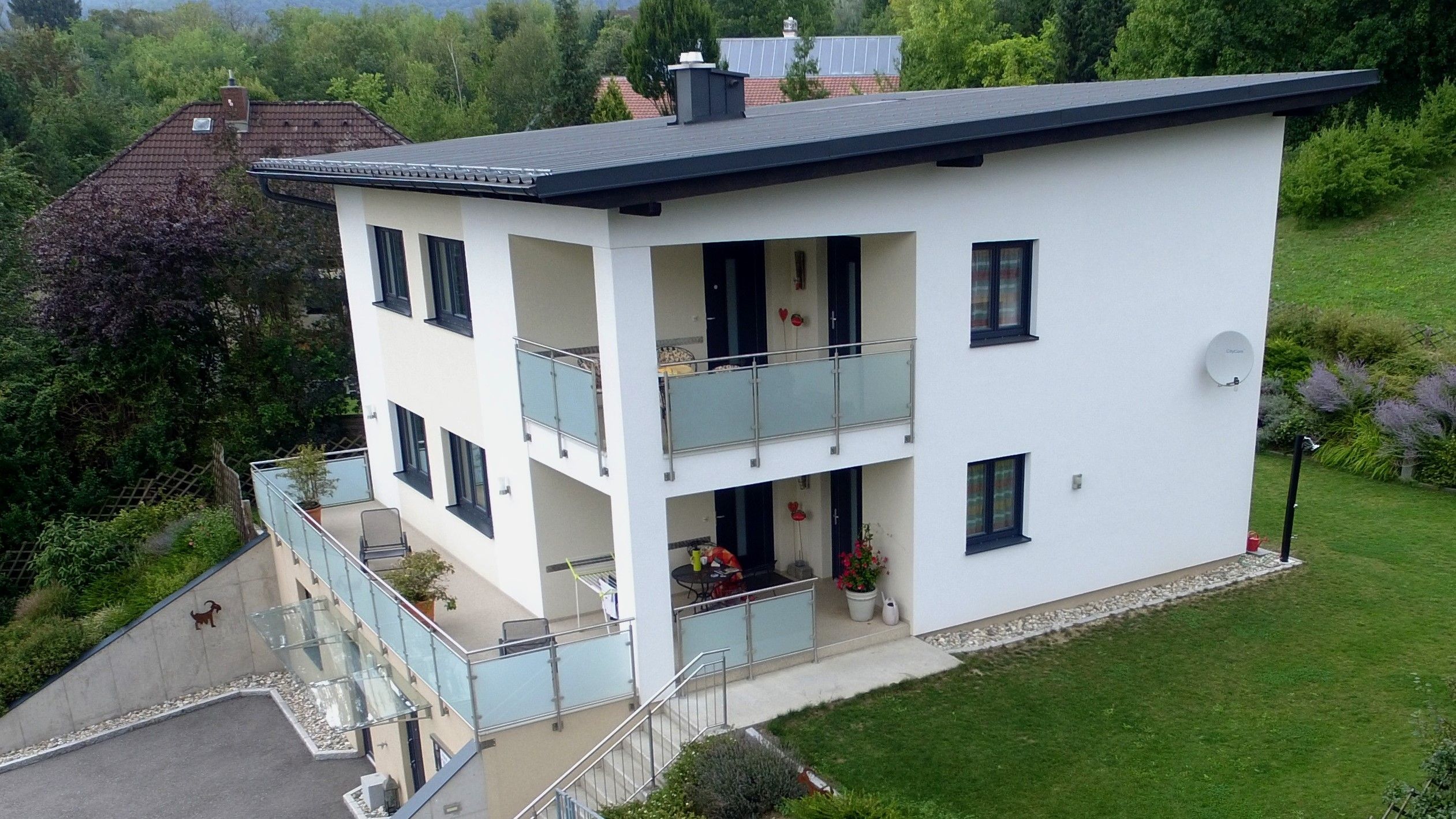 Záběr z dronu na moderní dvoupodlažní dům s balkonem a zahradou.