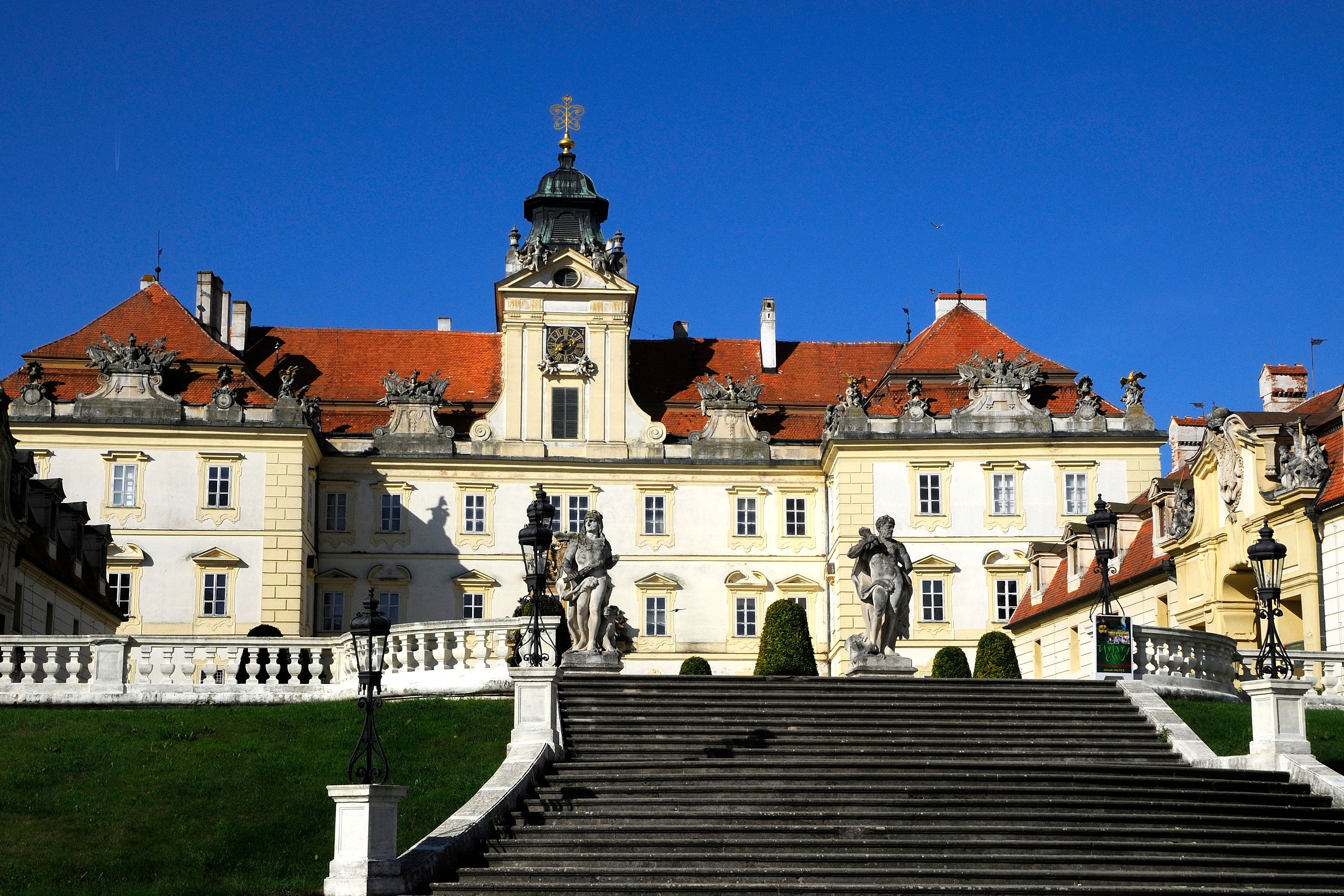 Pohled na valtický zámek zepředu se schody a sochami v popředí.