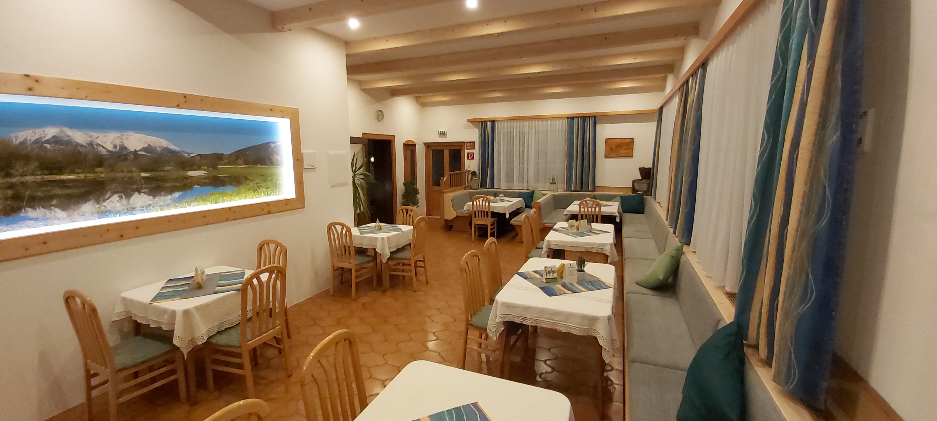 Útulná restaurace s dřevěným nábytkem a horským obrazem na stěně.