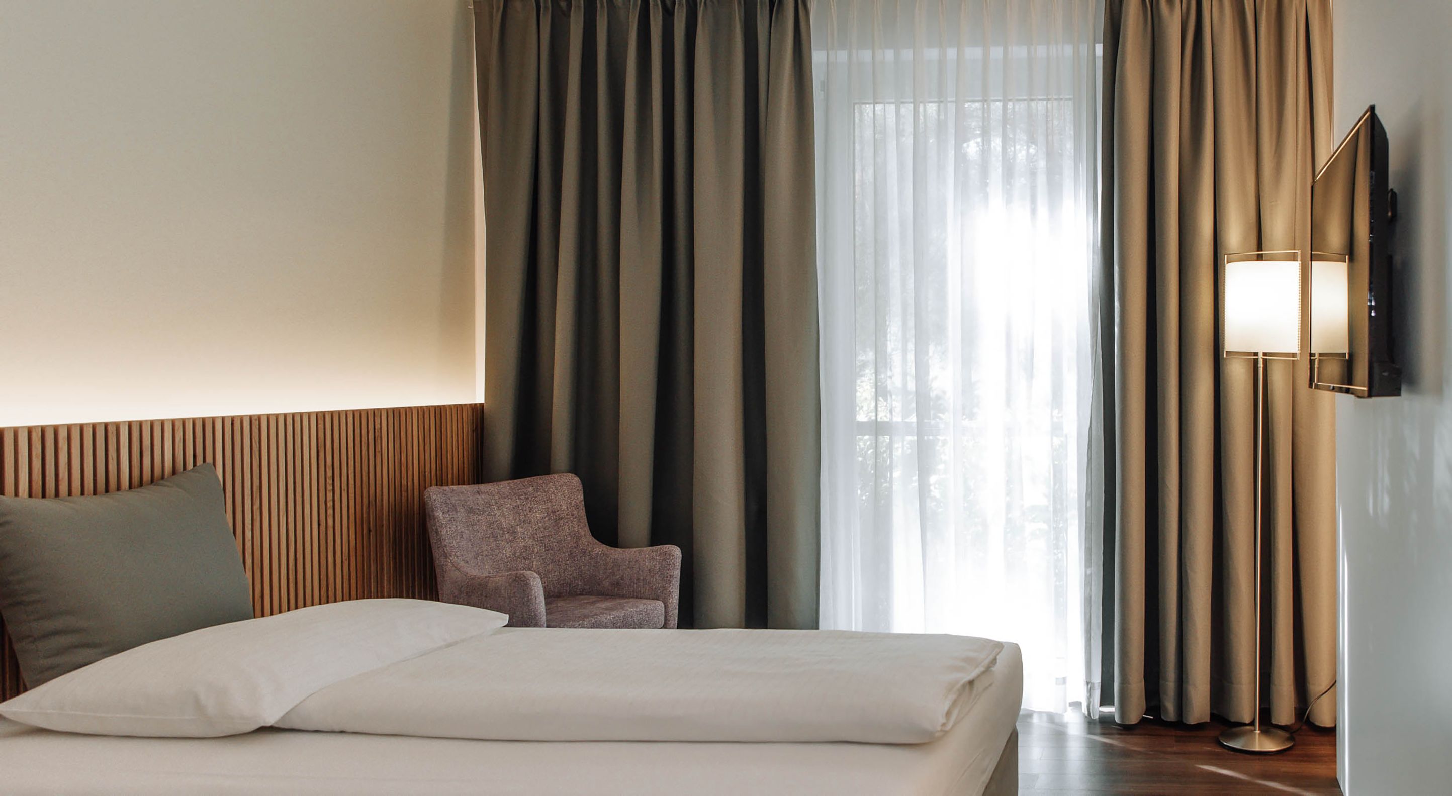 Moderní hotelový pokoj s postelí, křeslem a závěsy.