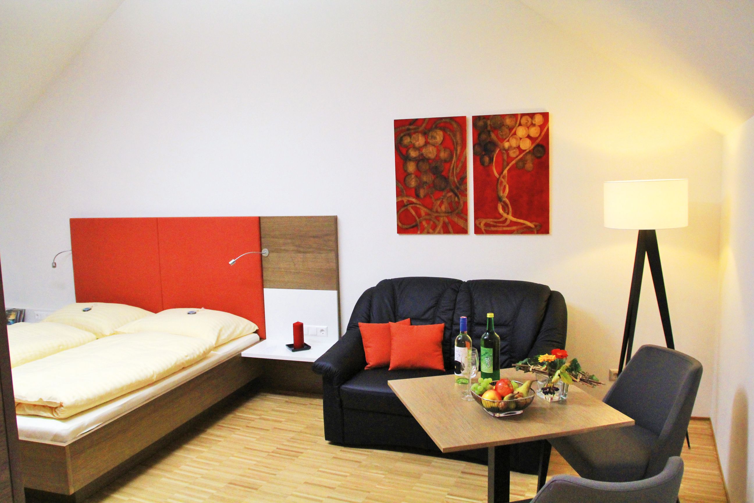 Útulný pokoj s manželskou postelí, pohovkou, stolem a stojací lampou.