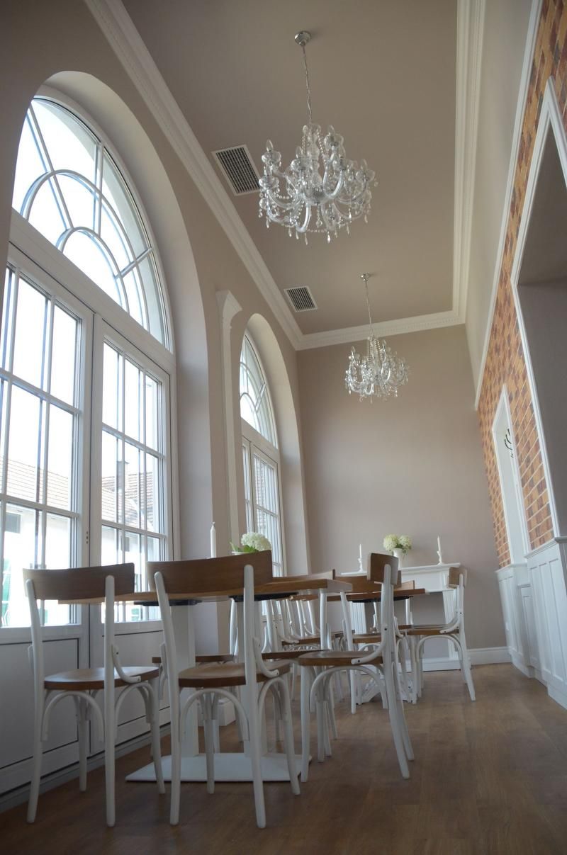 Elegantní pokoj s vysokými okny, lustry a dřevěným nábytkem.