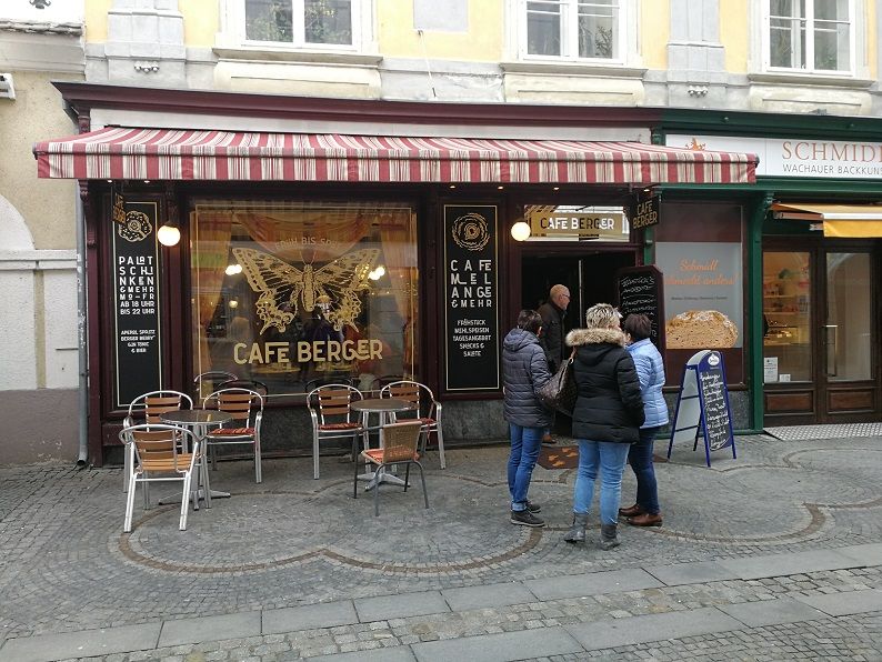 Pohled zvenčí na kavárnu Cafe Berger s posezením a lidmi před vchodem.