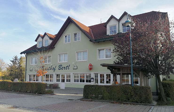 Dvoupatrová budova s nápisem "Gasthof Bertl", obklopená stromy a keři.