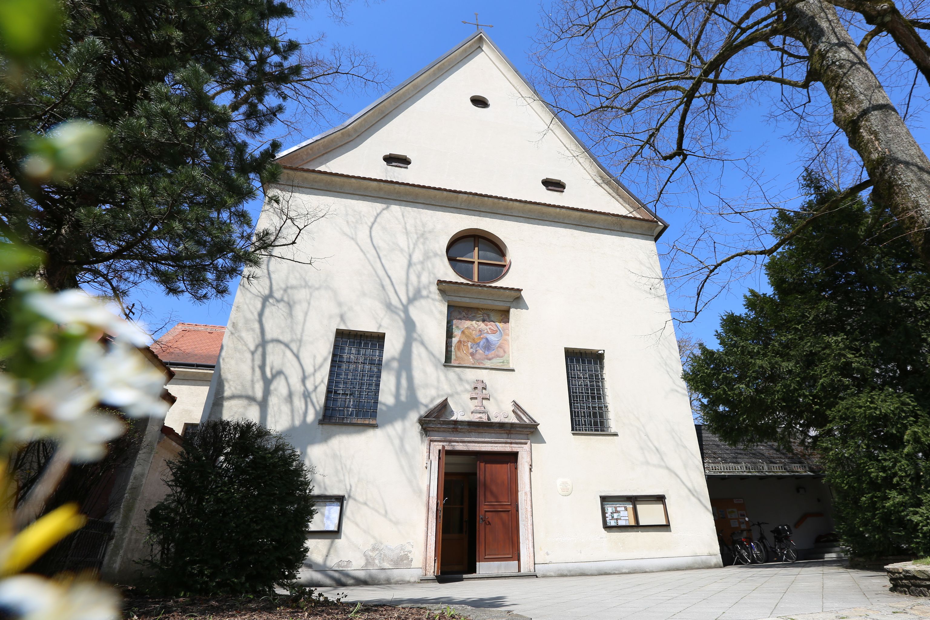 Průčelí kapucínského kostela s vchodem a okny, obklopené stromy.