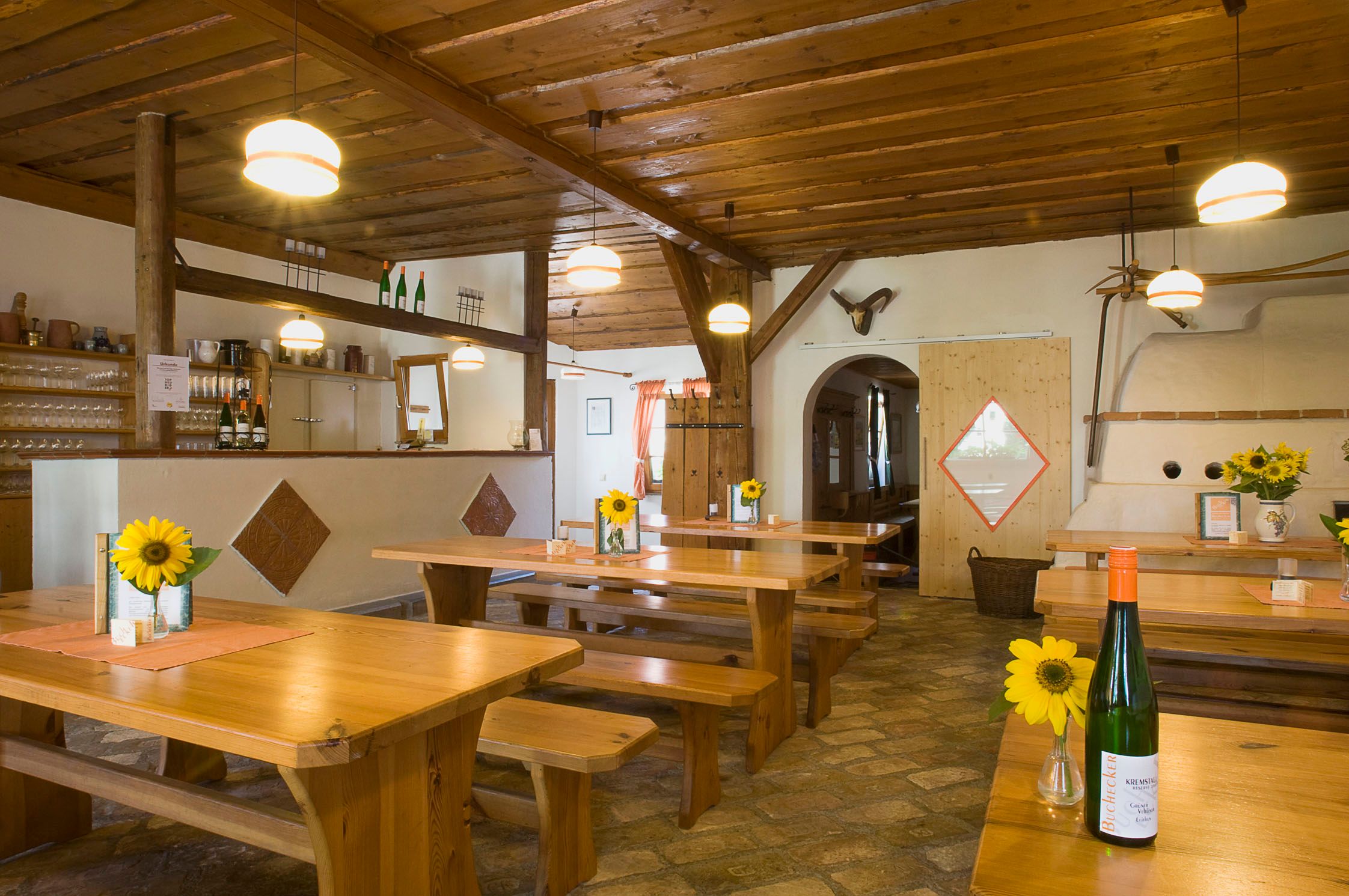 Pohled do interiéru tradiční vinárny s dřevěnými stoly, slunečnicemi a lahvemi vína.