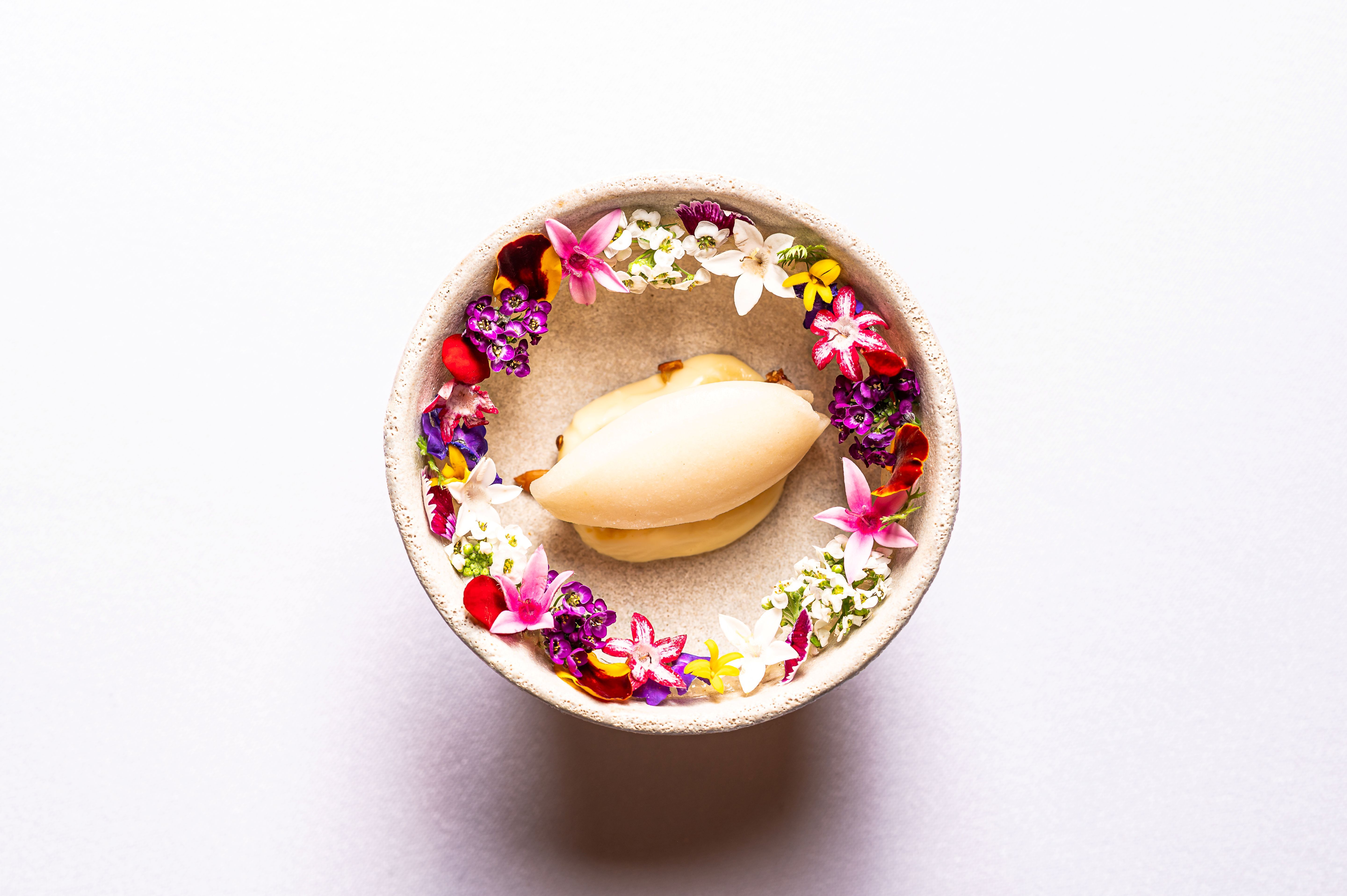 Dezert v misce obklopený barevnými jedlými květy.