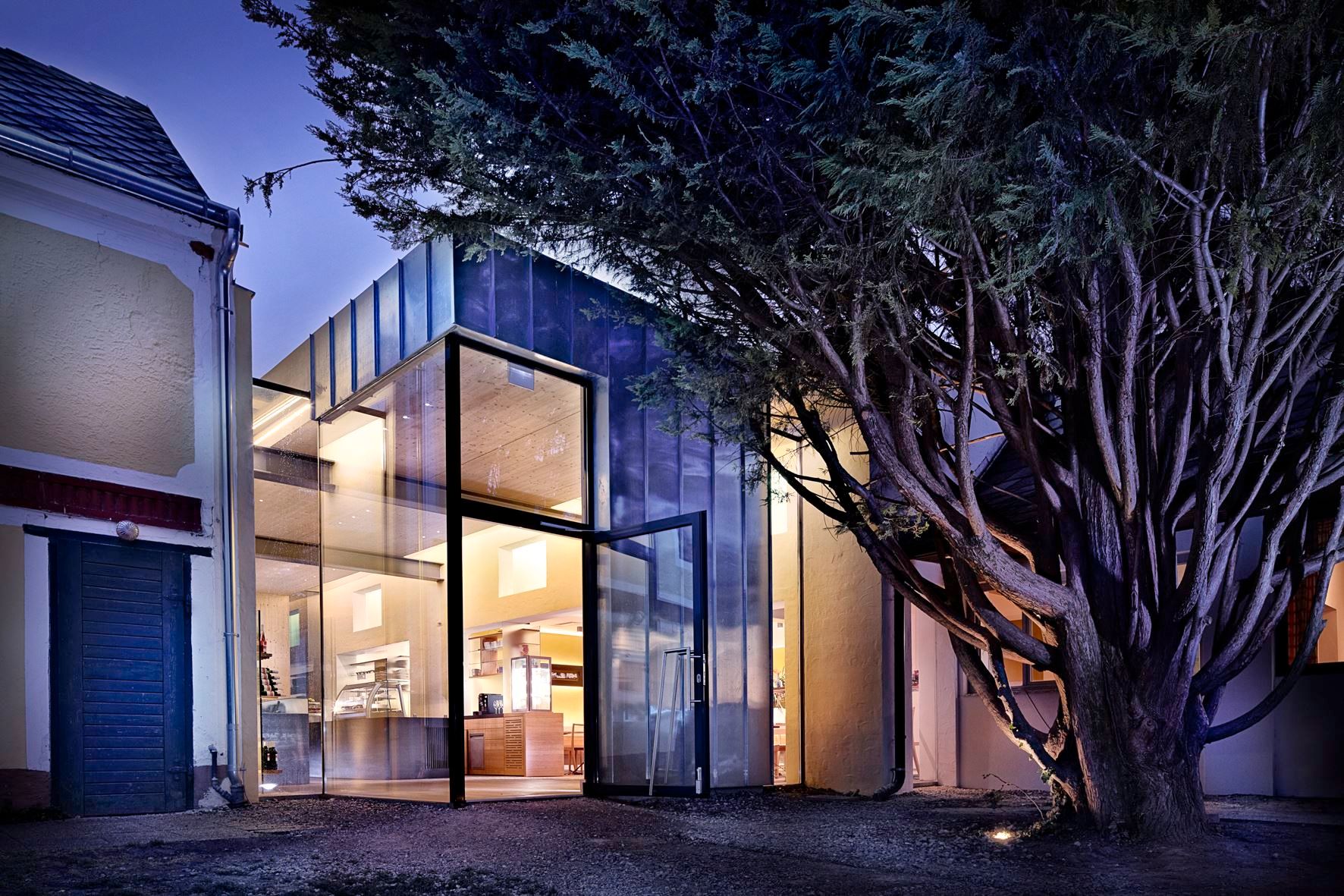 Moderní skleněná fasáda budovy v noci, obklopená stromy.