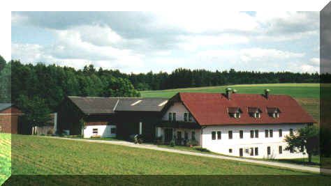 Tradiční statek s červenými střechami v venkovském prostředí, obklopený zelenými poli a lesy.