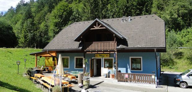 Modrá budova s dřevěným balkonem a terasou, obklopená stromy.